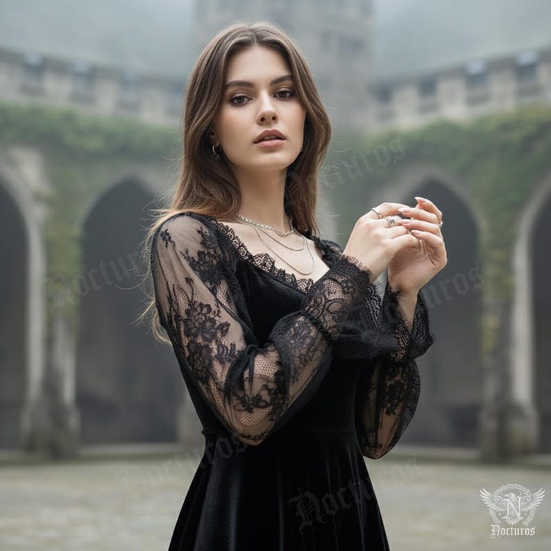 May include: A black velvet dress with long sleeves featuring intricate black lace detailing. The dress has a scoop neckline and a flowing skirt. The sleeves are sheer, showcasing the lace pattern. The background is a blurred outdoor setting with a stone building.