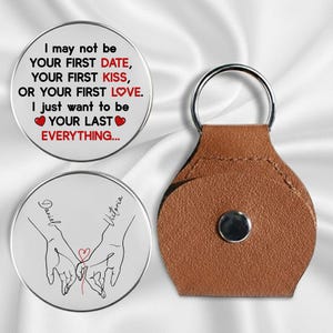 May include: A keychain with two round metal charms and a brown leather holder. One charm has the text "I may not be your first date..." and the other has two hands holding a heart. The keychain is a romantic gift.