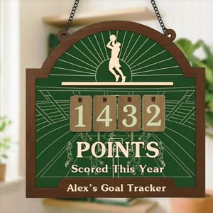 May include: Wooden basketball goal tracker with a green background and a brown frame. The scoreboard displays "1432 POINTS Scored This Year" and "Alex's Goal Tracker". A silhouette of a basketball player is at the top.