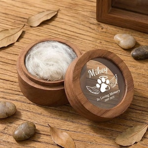 May include: A wooden pet memorial keepsake box with a clear lid. The lid is engraved with the name "Mikey", a paw print with wings, and the text "In Loving Memory 2009-2025". The box contains white pet fur.