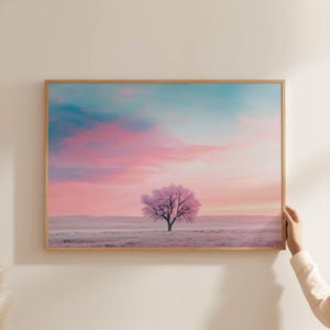 Könnte beinhalten: Gerahmter Landschaftsdruck mit einem einzelnen Baum mit rosa Blättern vor einem pastellfarbenen Himmel. Der Himmel geht von Türkis in Rosa und Orange über und erzeugt eine ruhige, farbenfrohe Szene. Der Druck ist in einem hellen Holzrahmen.