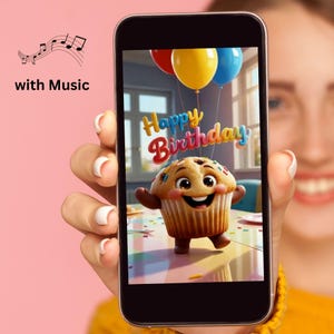 May include: A smartphone screen displays a digital illustration of a smiling, anthropomorphic cupcake character with colorful sprinkles. Above the cupcake, the text Happy Birthday appears in a stylized font, accompanied by red, yellow, and blue balloons.
