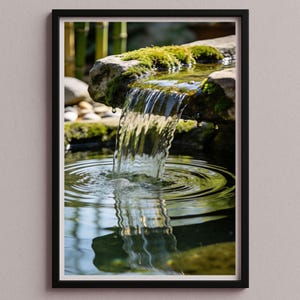 Puede incluir: Fotografía enmarcada de una pequeña cascada. El agua fluye desde una roca cubierta de musgo hacia un estanque, creando círculos concéntricos. Se ve bambú en el fondo. La imagen evoca una sensación de tranquilidad y belleza natural.