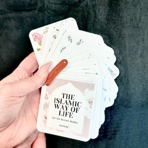 Puede incluir: Un mazo de cartas blancas con diseños florales y botánicos, sujetas por una etiqueta de cuero marrón que dice "Hand Made". Las cartas presentan el texto "THE ISLAMIC WAY OF LIFE" y están destinadas al musulmán devoto.