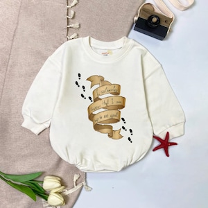May include: A white baby onesie with long sleeves. The front features a tan scroll with the text "I solemnly swear that I am up to no good" and black footprints. A red starfish is in the bottom right corner.