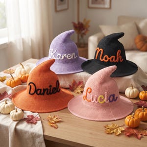 Può includere: Quattro cappelli da strega a punta nei colori viola, nero, arancione e rosa, ognuno con un nome ricamato sul davanti. Il cappello viola riporta il nome Karen, quello nero Noah, quello arancione Daniel e quello rosa Lucia in filato colorato.