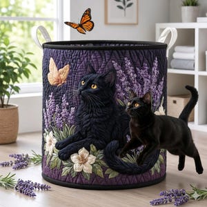 Puede incluir: Una cesta de lavandería redonda y acolchada con un diseño de gato negro y lavanda. La cesta presenta un borde negro, asas blancas y un fondo morado. Las mariposas y las flores blancas también forman parte del diseño.