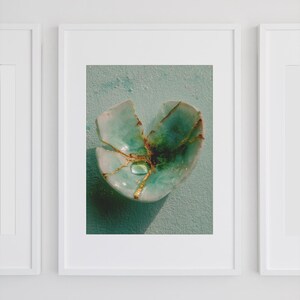 Peut inclure: Impression encadrée d'un bol en céramique turquoise cassé, réparé avec du kintsugi doré. Le bol présente une goutte d'eau au centre. Le fond est de couleur turquoise clair. L'image est dans un cadre blanc.