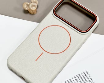 May include: A white phone case with a textured surface and a red circle design. The case has a black and orange trim. A small, beige decorative object is next to the phone case. The case is designed to protect a phone.
