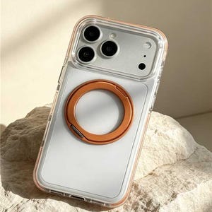 May include: Clear phone case with a copper-colored ring holder. The case has a clear border with a copper-colored trim. The phone case is on a light-colored, textured surface. The phone case has three camera lenses.
