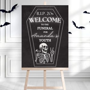 May include: A black and white sign on an easel with the text "R.I.P. 20s WELCOME TO THE FUNERAL FOR Amanda's YOUTH". A skeleton illustration is holding a cocktail and making a peace sign. Black bat decorations are in the background.