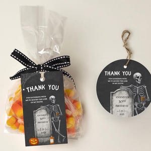 May include: A Halloween-themed gift bag filled with candy corn, tied with a black and white polka dot ribbon, and a matching tag. The tag features a skeleton, tombstone, and the words "Thank You". A second tag is also visible.
