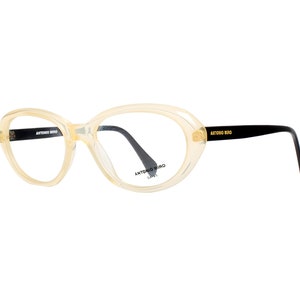 Puede incluir: Un par de gafas transparentes de color amarillo claro con patillas negras. Las patillas están etiquetadas con "Antonio Miro" en letras negras. Las gafas tienen una forma redondeada y ovalada.