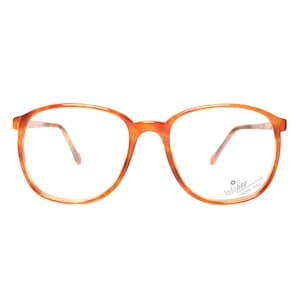 Puede incluir: Gafas de montura redonda con un patrón de carey en tonos naranja y marrón. Las monturas tienen un diseño clásico y las lentes son transparentes. Las patillas son de color marrón claro. Las gafas tienen una pequeña etiqueta en la lente derecha.