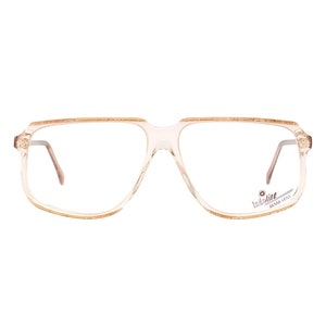 May include: A pair of clear, rectangular-shaped eyeglasses with a brown frame. The brand name "Indi-line" is printed on the right temple arm.
