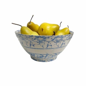 May include: A ceramic mixing bowl featuring a white base with a blue sponge-painted pattern and a solid horizontal band. The bowl is filled with five yellow pears, each with a brown stem, arranged inside the basin of the rounded vessel.