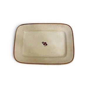 May include: A rectangular ceramic serving platter with a cream-colored base and a thin brown rim. The center of the platter features a small, dark brown botanical illustration of a three-leaf clover or shamrock design centered on the surface.