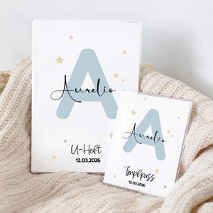 Könnte beinhalten: Zwei weiße Dokumentenhalter, einer groß und einer klein, mit einem hellblauen Buchstaben "A" und dem Namen "Aurelio" in Schreibschrift. Der größere Halter hat "U-Heft" und das Datum "12.03.2026". Der kleinere Halter hat "Impfpas" und das gleiche Datum.
