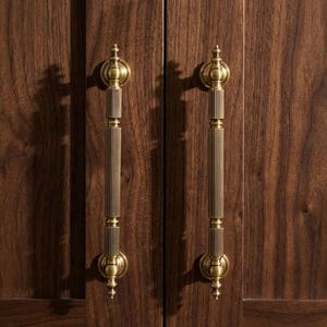 Puede incluir: Dos tiradores de armario de latón antiguo con diseño de estrías verticales. Los tiradores están montados en un armario de madera marrón oscuro. Cada tirador tiene una parte superior e inferior decorativas.