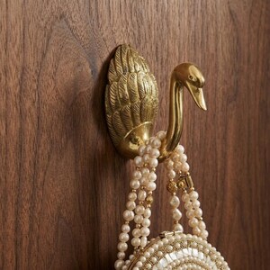 Gancho de pared decorativo de latón con forma de cisne para colgar abrigos y bolsas.