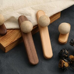 May include: A collection of wooden cabinet knobs with spherical stone accents. The knobs are in various shades of brown and natural wood, with a light-colored fabric and wooden box in the background. Dried flowers are in the foreground.