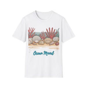 May include: White t-shirt with a beach design. The graphic shows seashells, coral, and the text "Ocean Mood" in blue. The design includes seashells, red coral, and green seaweed on a sandy beach.