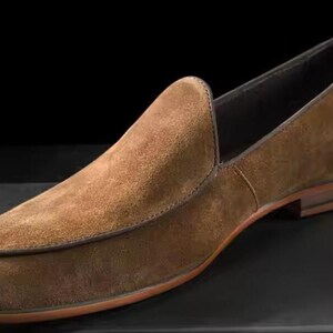 Puede incluir: Mocas&iacute;n de ante marr&oacute;n con punta redondeada y tac&oacute;n bajo. El zapato tiene un ribete cosido y suela de cuero. El dise&ntilde;o es sencillo y elegante, adecuado para diversas ocasiones.