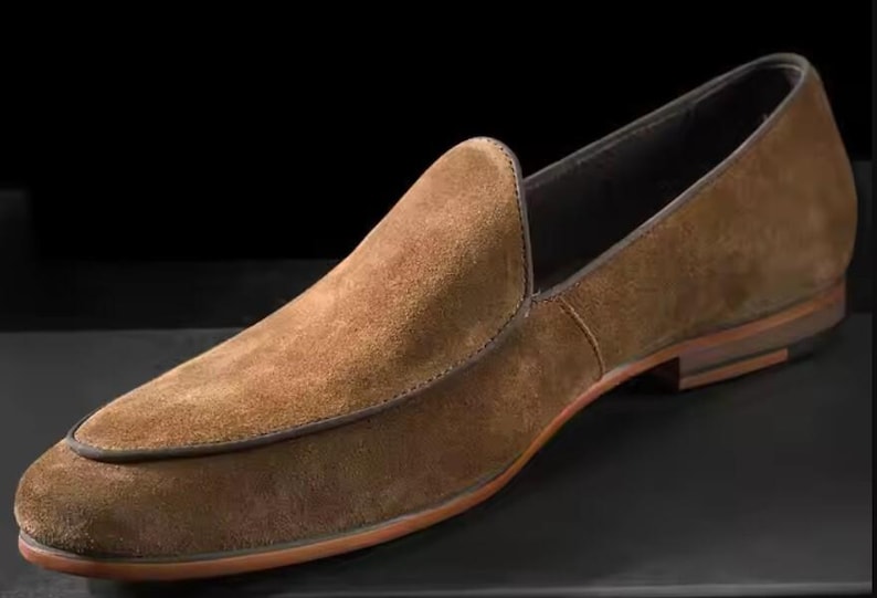 Puede incluir: Mocas&iacute;n de ante marr&oacute;n con punta redondeada y tac&oacute;n bajo. El zapato tiene un ribete cosido y suela de cuero. El dise&ntilde;o es sencillo y elegante, adecuado para diversas ocasiones.
