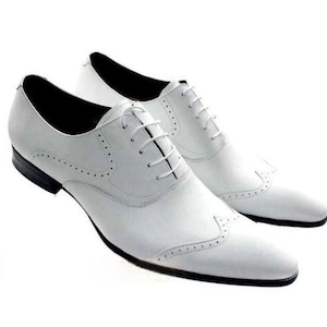 May include: A pair of white leather dress shoes with a classic Oxford design. The shoes feature a pointed toe, decorative perforations, and a lace-up closure. The soles are black.