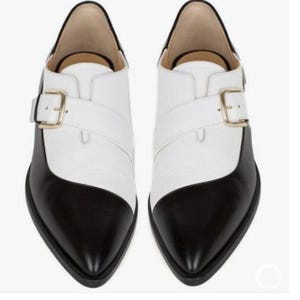 Pu&ograve; includere: Un paio di scarpe in pelle bicolore, con punta e tacco neri e tomaia bianca. Ogni scarpa presenta una fibbia color oro e una punta affusolata. Queste scarpe sono adatte per eventi formali o semi-formali.