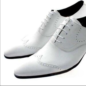 May include: A pair of white leather dress shoes with a classic Oxford design. The shoes feature a lace-up closure, decorative perforations, and a black sole. The shoes are designed for formal occasions.