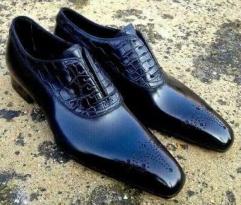 K&ouml;nnte beinhalten: Ein Paar gl&auml;nzende, schwarze Lederschuhe. Die Schuhe haben ein strukturiertes Muster auf dem Obermaterial und ein perforiertes Design an der Spitze. Die Schuhe sind formell und elegant.