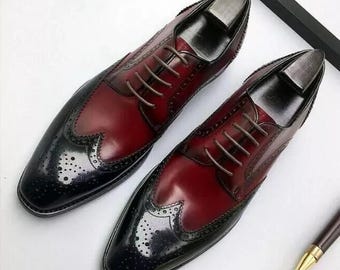 May include: A pair of two-tone leather dress shoes. The shoes feature a burgundy vamp and a black toe cap with decorative perforations. Brown laces and shoe trees are visible.