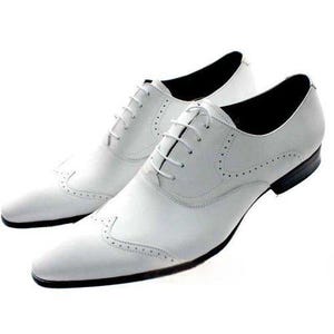 May include: A pair of white leather dress shoes with a classic wingtip design. The shoes feature a lace-up closure, a pointed toe, and black soles. The shoes are designed for formal occasions.