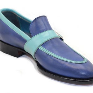 May include: A single blue leather loafer with a light blue accent strap and trim. The shoe has a black sole and heel, and a light blue interior. The design is a classic slip-on style.
