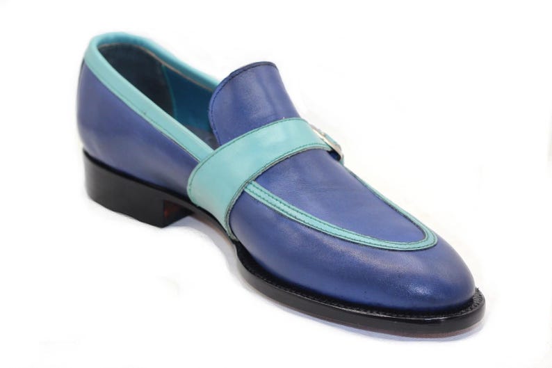 May include: A single blue leather loafer with a light blue accent strap and trim. The shoe has a black sole and heel, and a light blue interior. The design is a classic slip-on style.