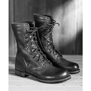 Puede incluir: Un par de botas de cuero negro con cordones, diseño de caña alta, múltiples ojales metálicos, punteras redondeadas y suela resistente. Las botas están confeccionadas con paneles de cuero texturizado y cordones negros a juego.