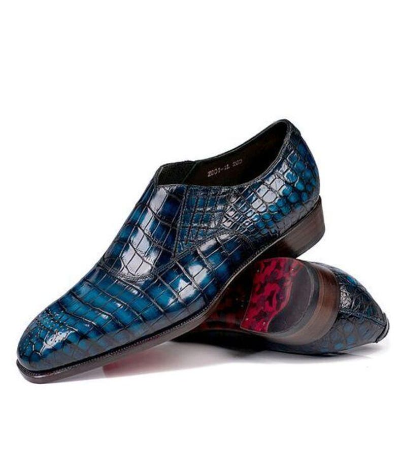 May include: A pair of blue leather dress shoes with a crocodile skin pattern. The shoes have a glossy finish and a dark brown sole. The sole of the shoe has a red and black pattern. The shoes are on a white background.