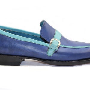May include: Blue leather loafer with a turquoise trim and strap. The shoe features a silver buckle and a black sole. A stylish, classic design.