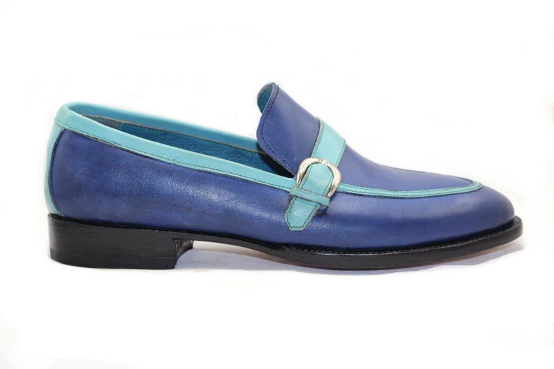 May include: Blue leather loafer with a turquoise trim and strap. The shoe features a silver buckle and a black sole. A stylish, classic design.
