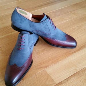 May include: A pair of two-tone dress shoes. The upper is a soft blue suede, with a burgundy leather toe cap and heel. The shoes have burgundy laces and decorative stitching. The soles are black.