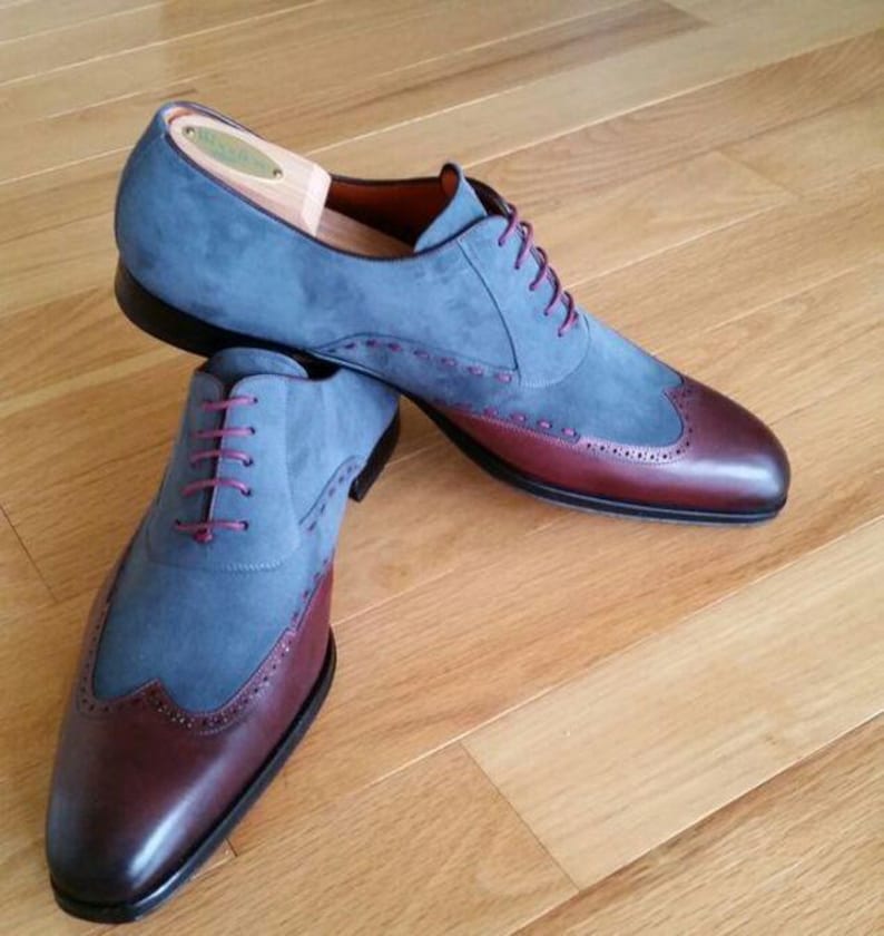 May include: A pair of two-tone dress shoes. The upper is a soft blue suede, with a burgundy leather toe cap and heel. The shoes have burgundy laces and decorative stitching. The soles are black.