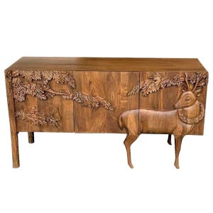 May include: A wooden cabinet with three doors and four legs. The cabinet is carved with a deer and foliage design. The deer is standing on the right side of the cabinet. The cabinet is brown.