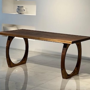 May include: A rectangular wooden dining table with a dark brown finish. The table is supported by two curved, oval-shaped legs. The table's dimensions are approximately 72 inches long, 36 inches wide, and 30 inches high.