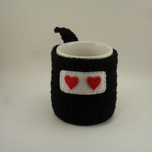May include: Black crocheted mug cozy with a white felt patch and two red felt hearts.
