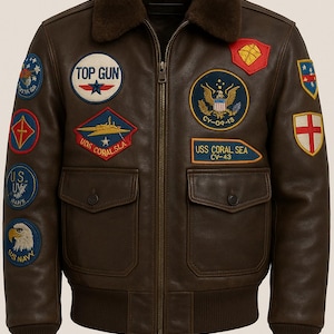 May include: Brown leather bomber jacket with multiple embroidered patches, including "TOP GUN" and "USS CORAL SEA CV-43". Features a brown fur collar, a zip-up front, and two front pockets. The jacket has a ribbed hem and cuffs.