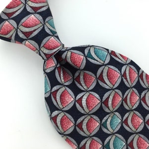 May include: A navy blue silk tie with a geometric pattern of red, silver, and teal circles and squares.