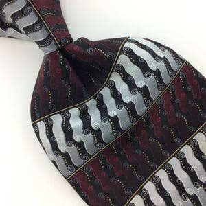 May include: A black, burgundy, and silver patterned silk tie with a geometric design. The pattern features swirls and lines.