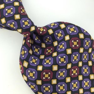 May include: A silk tie with a geometric pattern in shades of purple, gold, burgundy, and black.