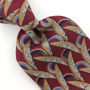 May include: A red silk tie with a geometric pattern of brown, blue, and white. The pattern features curved lines and dots.